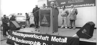 Na época da reunificação alemão, 1990, trabalhadores do setor metalúrgico e eletroeletrônico de Berlim e Brandemburgo protestam em frente à Treuhandanstalt pela preservação dos empregos, em 28 de novembro de 1990. À esquerda, o prefeito Walter Momper acompanha o discurso de Manfred Foede, representante da IG Metall. Foto: Wikipedia