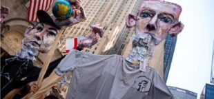 Obras de arte representando bilionários Mark Zuckerberg e Elon Musk com as mãos ensanguentadas carregando globos desfilam por Manhattan no protesto climático "Façam os Bilionários Pagarem", em 20 de setembro de 2025, em Nova York. | Angelina Katsanis / AP